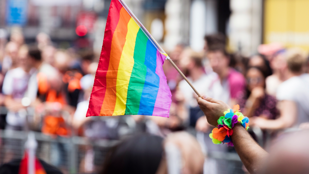Mannenhand zwaait met regenboogvlag bij een Pride