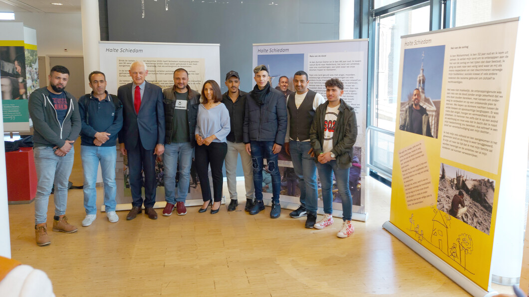 Burgemeester Lamers temidden van een groep vluchtelingen, wiens verhalen verteld worden in de tentoonstelling 'Halte Schiedam'