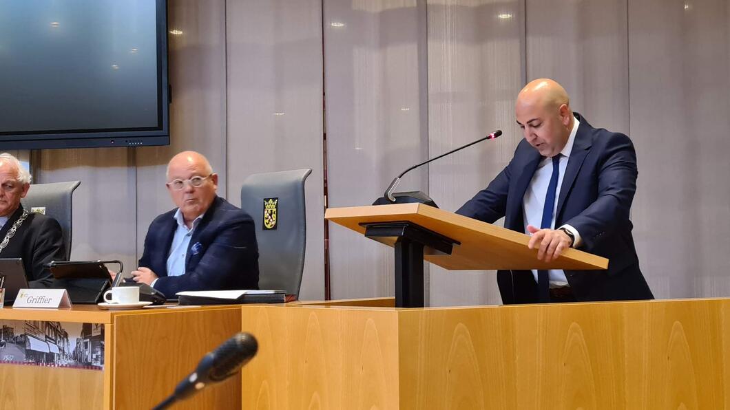 GroenLinks-raadslid Serkan Kılıçkaya spreekt de raad toe. Ook in beeld zijn burgemeester Lamers en interim-griffier Hermans.