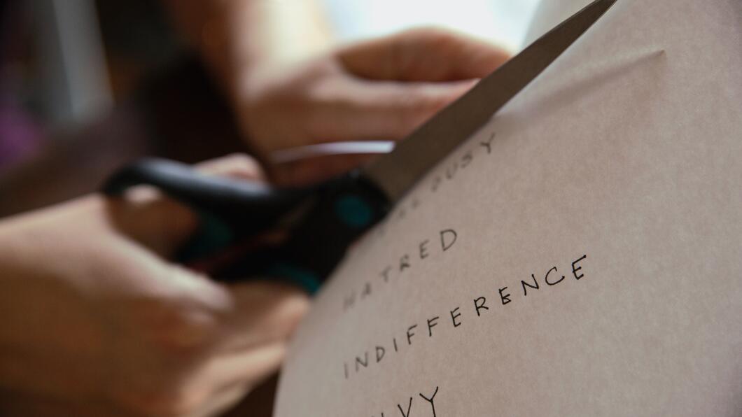 Persoon knipt in een papier waar woorden als 'jealousy', 'hatred' en 'indifference' op staan 