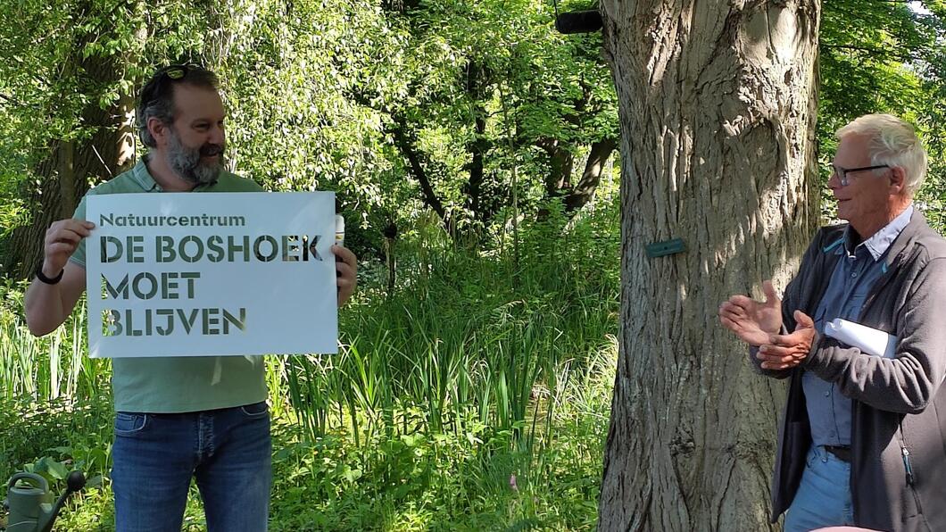 Yorick geeft Wout een krijtsjabloon met de tekst "Natuurcentrum de Boshoek moet blijven"
