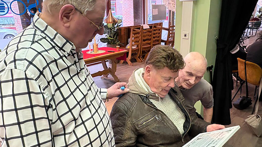 Henk van den Broek laat het certificaat zien aan mede-vrijwilligers