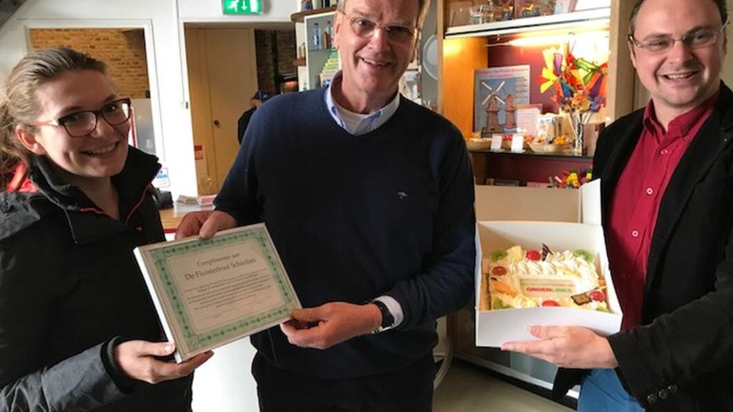 GroenLinks-raadsleden Katinka de Rover en Jeroen Ooijevaar reiken de taart en een oorkonde uit aan voorzitter Ad van Leeuwen van de Stichting Rondvaarten Schiedam
