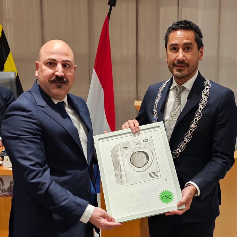 Serkan en de burgemeester laten het "Wenswerk" zien dat de burgemeester zojuist van GroenLinks kreeg aangeboden.
