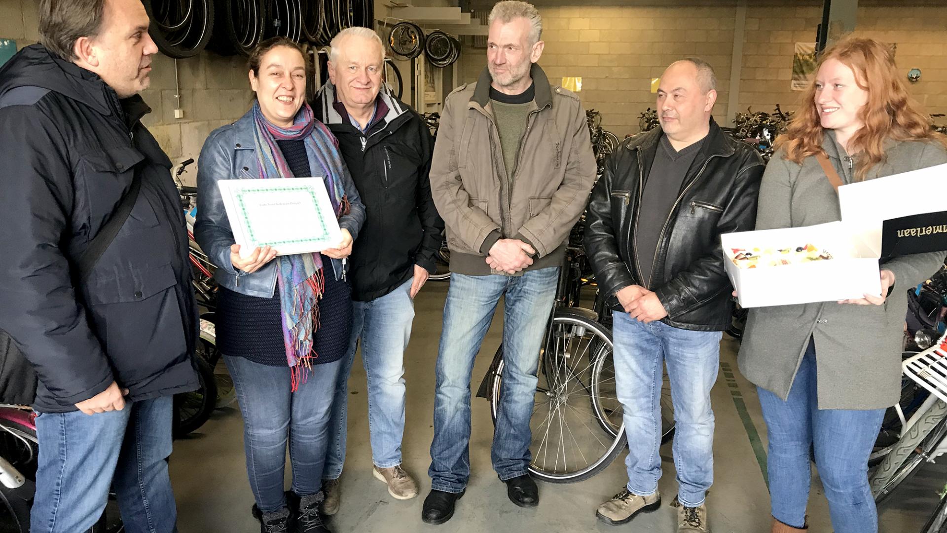 Statenkandidaat Menno Siljee spreekt Debbie, Frans (beiden LETS Ruilwinkel), fietsenmaker Michel en leermeester Marcel toe, terwijl Shanna klaarstaat om de complimententaart te overhandigen